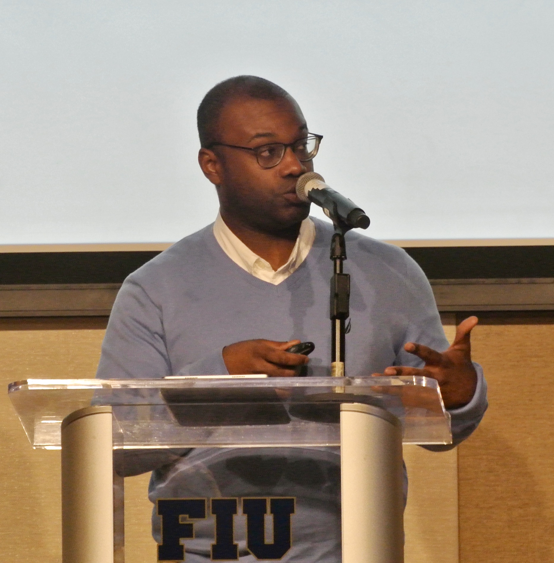 Black man in blue sweater standing at a podium giving a lecture